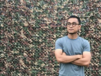 Young man standing with arms crossed against camouflage pattern