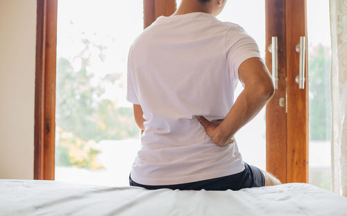 Rear view of man standing on bed