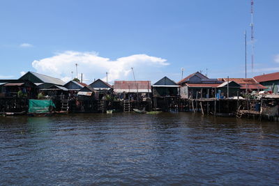 Houses by river against buildings against blue sky