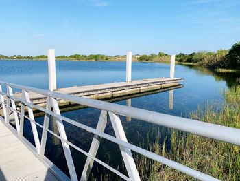 Wooden railing by lake against blue sky