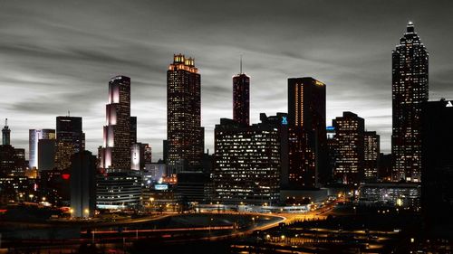 Illuminated buildings in city against cloudy sky