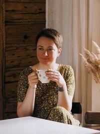 Portrait of young smiling woman with short hair at home with a cup of coffee or tea in the morning.
