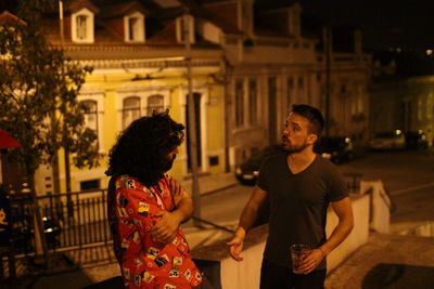 Young man holding drink while talking to friend on street at night