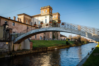 Arch bridge over river by buildings against sky