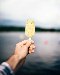 Close-up of hand holding ice cream against lake