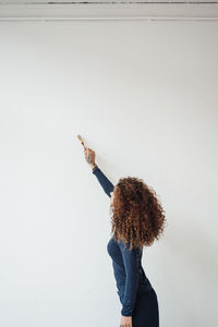 Young woman with curly hair using paintbrush on white wall