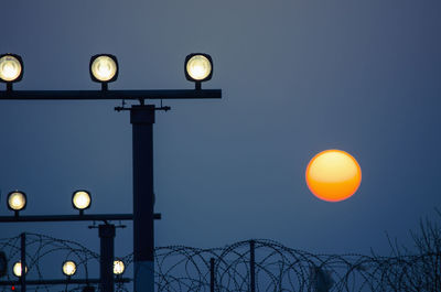 Low angle view of illuminated guiding lights against sun during sunset