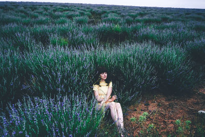 Young woman sitting on field by plants