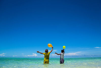 Rear view of children with balloons standing at beach against clear blue sky