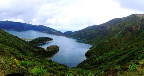 Scenic view of lake amidst grassy mountains against cloudy sky