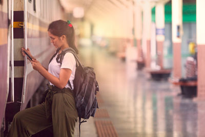 Side view of young woman using mobile phone while entering train at railroad station