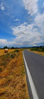 Empty road amidst field against sky