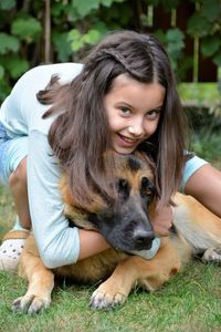 Portrait of happy girl embracing dog on grass