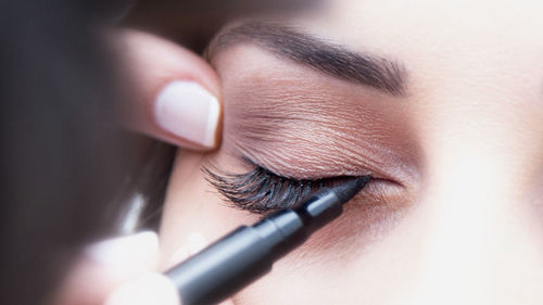 Close-up of cropped make-up artist applying eyeliner on woman