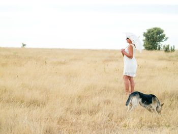 Woman with dog holding umbrella while standing on field against sky