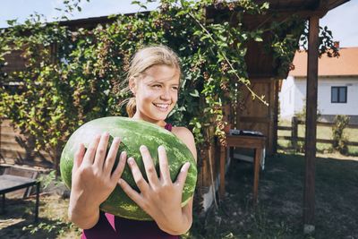 Cheerful girl holding watermelon while standing in yard