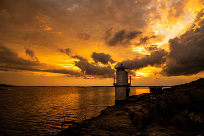 Lighthouse by sea against sky during sunset