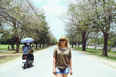 Portrait of smiling woman standing on road against trees