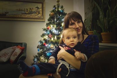 Portrait of cute girl holding christmas tree at home