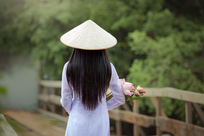 Rear view of woman wearing asian style conical hat against trees