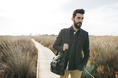 Mid adult man walking on boardwalk against sky