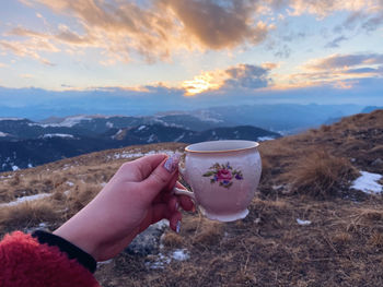 Midsection of person holding ice cream against mountains during sunset