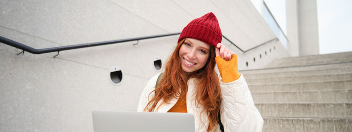 Rear view of woman using mobile phone while standing against wall