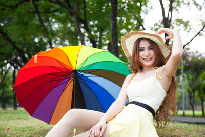 Close-up of young woman wearing hat while sitting on grass field by umbrella