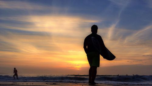 Silhouette of people standing on beach at sunset