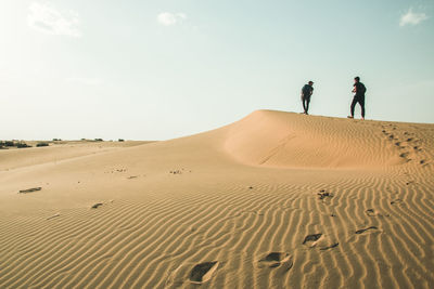 People on sand dune in desert against sky
