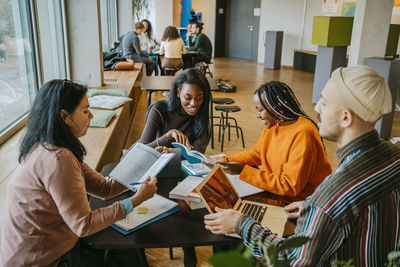 Smiling female students studying together with friends sitting table in university cafeteria