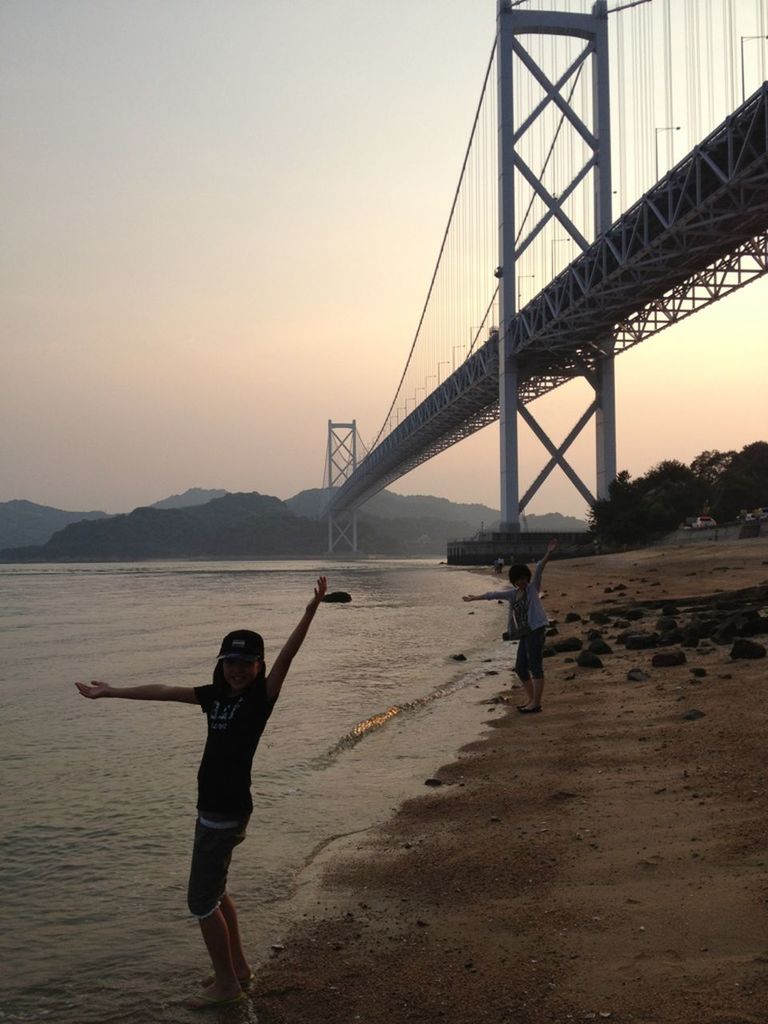 bridge - man made structure, connection, water, built structure, architecture, lifestyles, suspension bridge, clear sky, engineering, leisure activity, river, bridge, full length, rear view, standing, tourism, travel, travel destinations