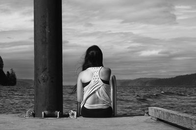 Rear view of woman sitting by sea against sky