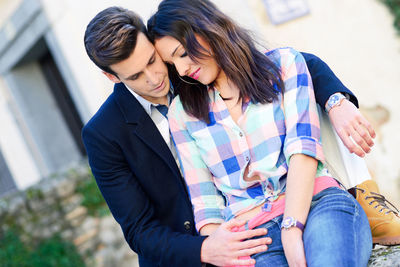 Young couple sitting on retaining wall against building