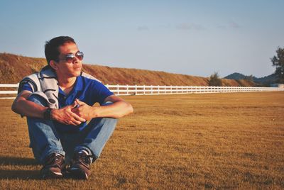 Young man wearing sunglasses sitting on field against sky