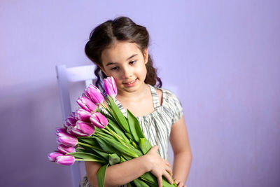Beautiful little girl with a bouquet of tulips, against the background of a purple wall