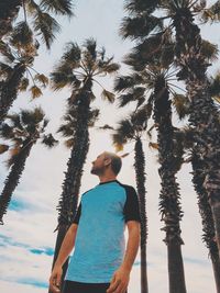 Rear view of man standing by palm trees against sky