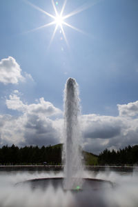 Fountain in lake at park against sky on sunny day