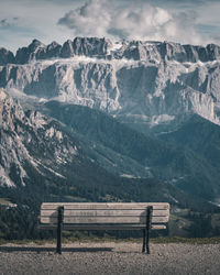 Empty bench on snowcapped mountains against sky