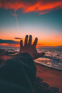 Cropped of hand against sea during sunset