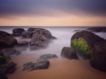 Rocks on sea shore against sky during sunset