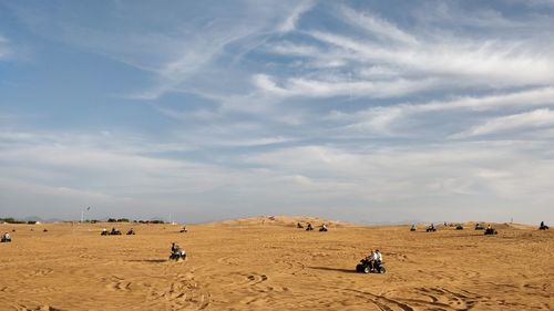 People on sand dune in desert against sky