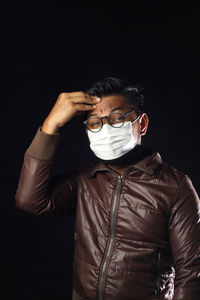 Portrait of man with headache standing against black background