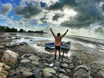 Rear view of man with arms raised standing on rock against sea at beach