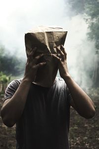 Man wearing paper bag while standing in forest