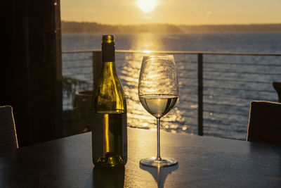 Wine bottle and glass on table against sea during sunset