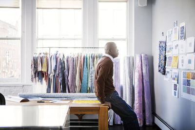 Side view of male fashion designer looking at designs on wall in workshop