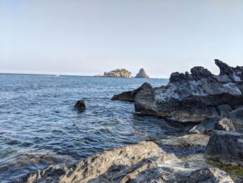 Rocks by sea against clear sky