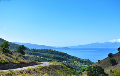 Scenic view of sea and mountains against clear blue sky