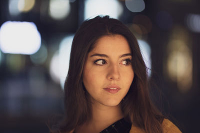 Close-up of young woman looking away while standing outdoors at night